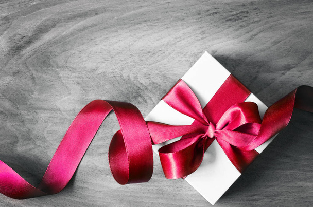 White gift box and red ribbon with tag on wood background. Vintage gift box on wooden board with space for text. - Photo, Image