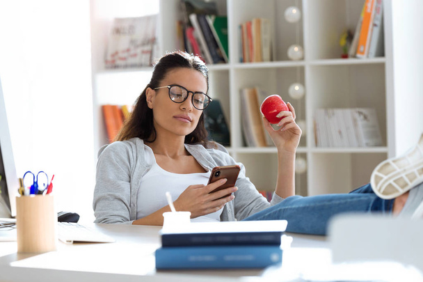 Genç ve güzel bir iş kadını ofiste onun cep telefonu yerken kırmızı elma kullanarak çekim. - Fotoğraf, Görsel
