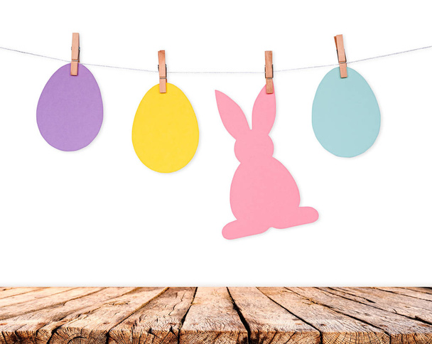 Mesa de madera y huevos y conejos guirnalda de decoración en la pared blanca. Fondo de vacaciones de Pascua
 - Foto, Imagen