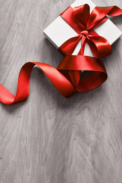Белая подарочная коробка и красная лента с биркой на деревянном фоне. Винтажный подарочный бокс на деревянной доске с местом для текста
. - Фото, изображение