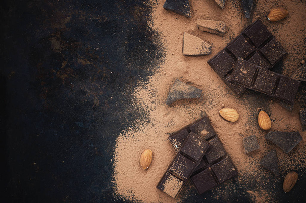 Chocolate on dark vintage background with cocoa powder and almonds.Top view.Copy space. - Foto, afbeelding