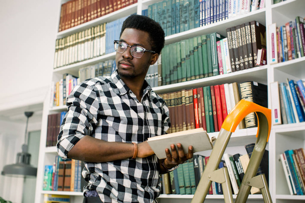 Молодой афроамериканский студент выглядит расслабленным и улыбающимся, прислонившись к стремянке.
 - Фото, изображение