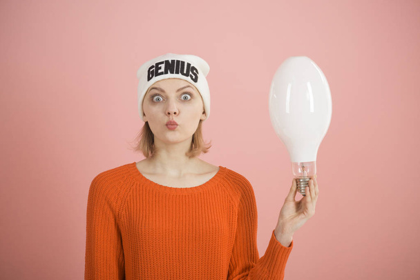 It all starts with an new idea. Girl genius got bright idea. Surprised woman hold light bulb. A genius idea came into her head. Sensual woman wear hat with genius word - Фото, изображение
