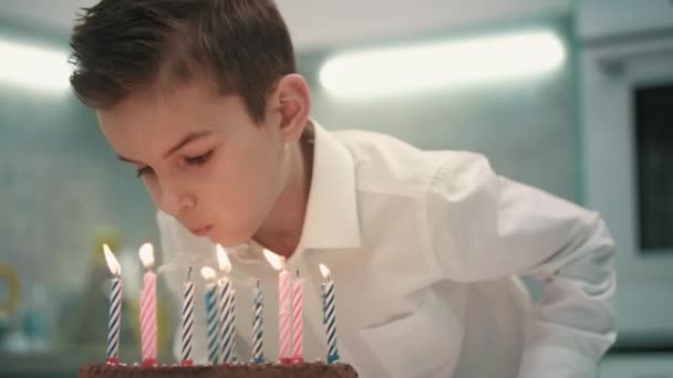Chłopiec Dmuchanie świeczki na tort urodzinowy. Zadowolony urodziny chłopiec dmuchanie na płomień świecy - Materiał filmowy, wideo