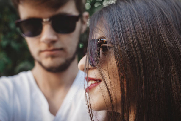 Stylish hipster couple in sunglasses posing and making cool selfie. Happy family couple in love making self portrait and embracing in evening summer city. - Photo, Image
