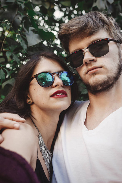 Stylish hipster couple in sunglasses smiling and making cool selfie. Happy family couple in love making self portrait and posing in evening summer city. Vacation  and travel together - Photo, Image