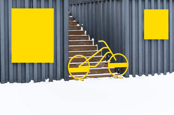 Dans la neige entre les garages avec boucliers jaunes se dresse un vélo et bloque l'entrée de l'escalier
 - Photo, image