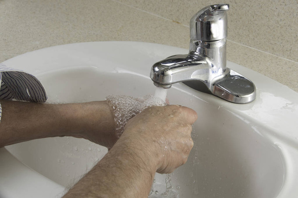 Человек, намыливающий руки для гигиены в раковине ванной комнаты
 - Фото, изображение