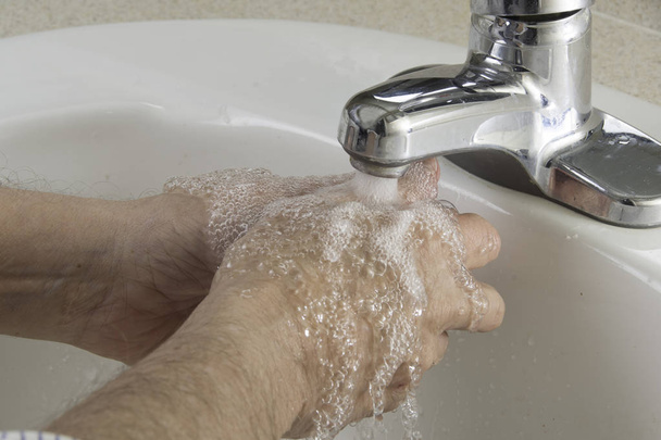 Человек, намыливающий руки для гигиены в раковине ванной комнаты
 - Фото, изображение