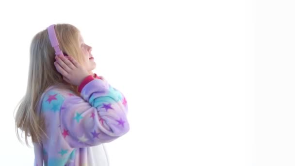 moderne mode - mooi blond meisje luistert naar muziek met hoofdtelefoons en dansen op een witte achtergrond in kigurumi pyjama - geïsoleerd op wit - Video