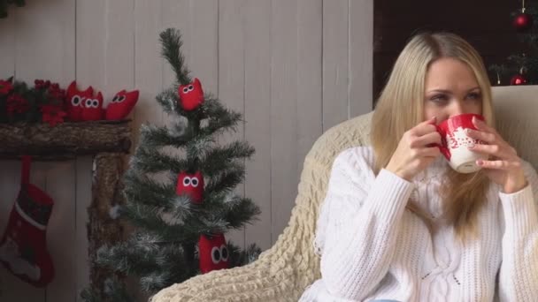 Woman sitting in a chair and drinking coffee or tea on the background of the Christmas interior. - Footage, Video