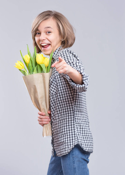 Beautiful Girl with Bunch of Flowers on gray background. Smiling Child with Bouquet of yellow Tulips as a Gift. Happy Mothers, Birthday or Valentines Day. - Zdjęcie, obraz