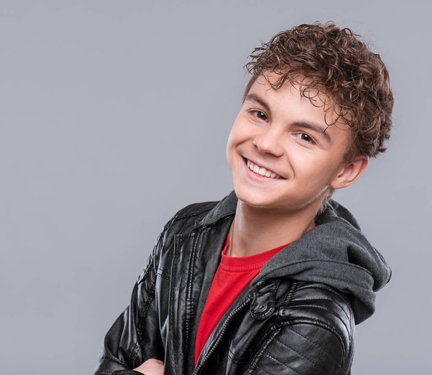 Portrait of a Handsome brutal Teen Boy in a black Leather Jacket. Smiling fashion Child Model posing on a gray background. Funny Teenager looking at Camera.  - Foto, Bild