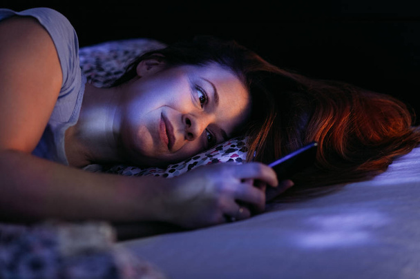 Молода жінка використовує смартфон в ліжку вночі
 - Фото, зображення