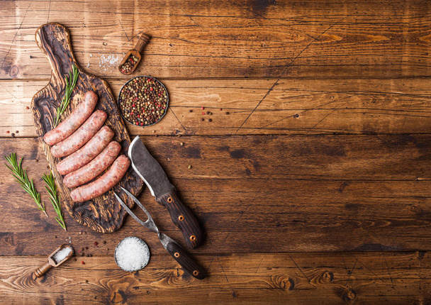 rohe Rind- und Schweinewurst auf altem Schneidebrett mit Vintage Messer und Gabel auf hölzernem Hintergrund. Salz und Pfeffer mit Rosmarin. - Foto, Bild