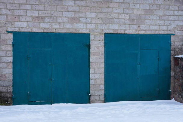 μπλε μεταλλικό πύλες σε ένα γκρίζο τοίχο γκαράζ έξω από το λευκό χιόνι - Φωτογραφία, εικόνα