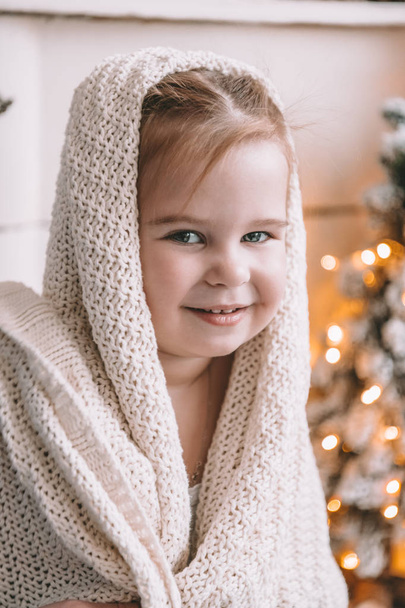 Симпатична маленька дівчинка вкрита великою плед або шарф вдома
 - Фото, зображення
