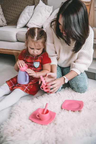 Happy loving family. Mother and her daughter girl play tea-party and drink tea from cups in children room. Funny mom and lovely child having fun indoors - Zdjęcie, obraz
