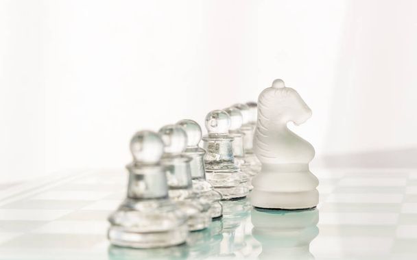 Glass chess pieces are set up in a line on the glass chess board. Pawns are standing behind their knight. - Photo, Image