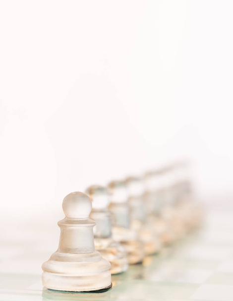 Piezas de ajedrez de vidrio se colocan en una línea en el tablero de ajedrez de vidrio. Uno de los peones se destaca entre los otros cuando desaparecen en el fondo
. - Foto, Imagen