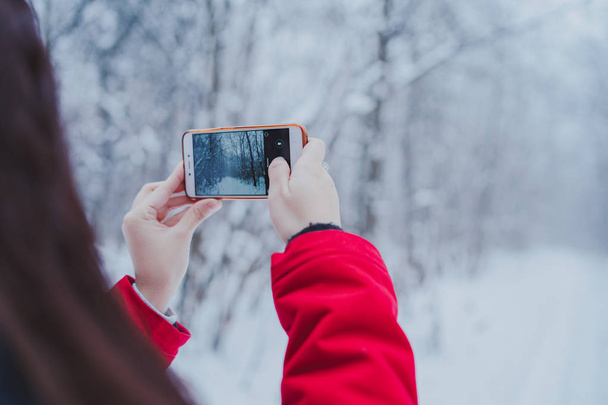 Girl taking pictures on a smartphone in the woods in the winter. Woman walking in the forest - Fotó, kép