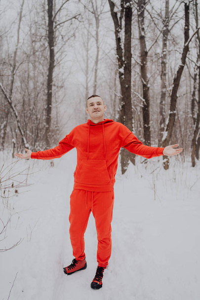 Crazy guy posing in the forest in the winter, on the background of snow and trees. A man in a red tracksuit walking in the fresh air. Concept: walking and training outdoors in the cold - Foto, Bild