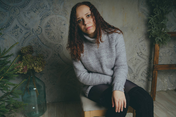 A young girl in a sweater posing against a gray wall. Woman dressed in warm sweater, street style clothing. Clean skin, long hair - Foto, immagini
