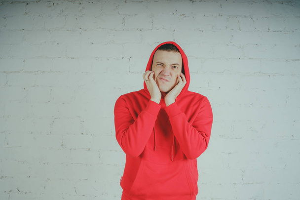 Handsome guy posing by a brick wall. Crazy man in a red hoodie - Fotó, kép