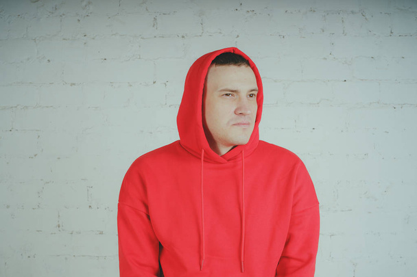Handsome guy posing by a brick wall. Crazy man in a red hoodie - Foto, afbeelding