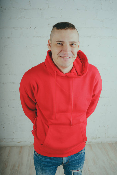 Handsome guy posing by a brick wall. Crazy man in a red hoodie - Fotografie, Obrázek