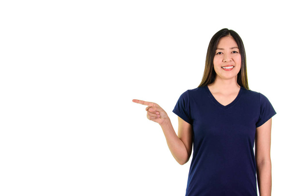 Νεαρή γυναίκα της Ασίας σε μπλε πουκάμισο, χαμογελώντας και δείχνοντας με το δάχτυλο στο χώρο σε λευκό φόντο. - Φωτογραφία, εικόνα