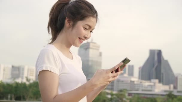 fröhliche asiatische Touristenbloggerin, die ihr Smartphone zur Orientierung benutzt und auf der Lagekarte sucht, während sie auf der Straße in der Innenstadt unterwegs ist. Lifestyle Rucksack touristisches Reisekonzept. - Filmmaterial, Video