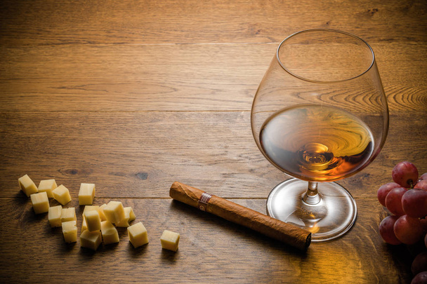 Bicchiere di cognac e sigaro con spuntino sul tavolo in legno con tagliere in pietra. Vista dall'alto con spazio di copia
 - Foto, immagini