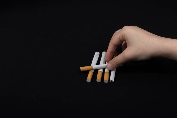 Hand hält gekreuzte Zigaretten auf schwarzem Hintergrund - Foto, Bild