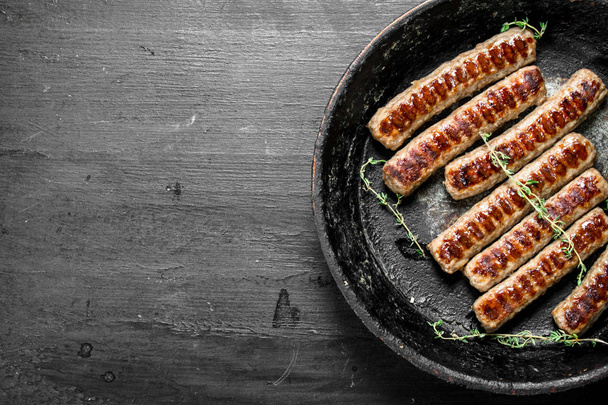 Жареные сосиски на сковороде с тимьяном. На фоне черной доски
. - Фото, изображение