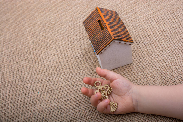 Pequeña mano sosteniendo una llave retro por una casa modelo sobre un fondo de color marrón
 - Foto, Imagen