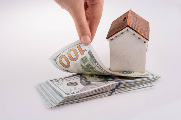 Mano humana sosteniendo billetes de dólar americano al lado de una casa modelo sobre fondo blanco
 - Foto, Imagen