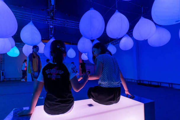 Visitors sit under illuminated giant raindrop-shaped installations at an interactive installation exhibition held to call on public care of those suffering from autism in Shanghai, China, 14 July 2016. - Photo, image