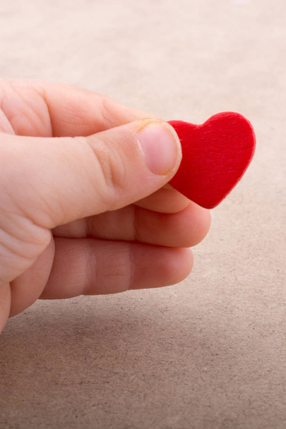 Kis piros színű szív alakja a kezében világosbarna háttér - Fotó, kép