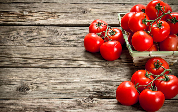 Ripe tomatoes in a basket. On a wooden background. - Фото, изображение