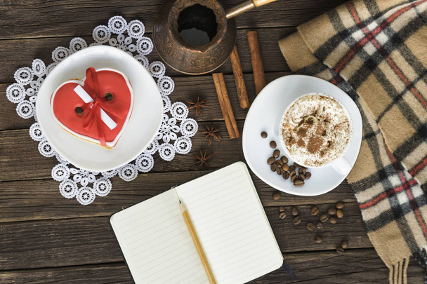 Fincan kapuçino, kalp kurabiye genişliği kahverengi ahşap bir masa üzerinde mesaj, defter, kalem ve kahve kap şeklinde. Tatil planlama - Fotoğraf, Görsel