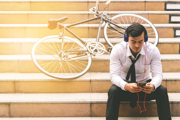 Biznesmen relaksuje się słuchając muzyki z rowerem na boku - Zdjęcie, obraz