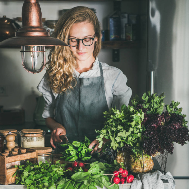 Fall seasonal vegetarian, vegan dinner cooking. Woman in apron and glasses cutting herbs and vegetables on concrete kitchen counter, square crop. Slow food, comfort food, healthy diet, clean eating - Foto, Imagen