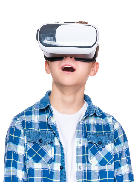 Happy teen boy wearing virtual reality goggles watching movies or playing video games, isolated on white. Cheerful teenager looking in VR glasses. Funny child experiencing 3D gadget technology. - Фото, изображение