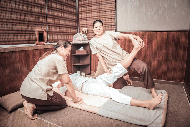 Positive Asian woman raising her clients leg up - Foto, afbeelding