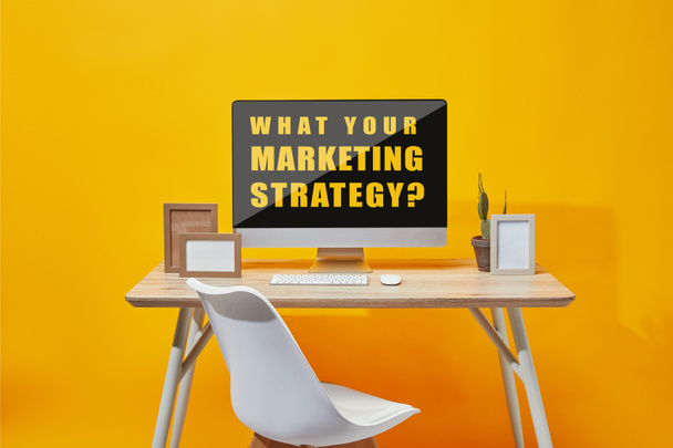 Computador com o que sua estratégia de marketing pergunta na tela na mesa de madeira no fundo amarelo
 - Foto, Imagem