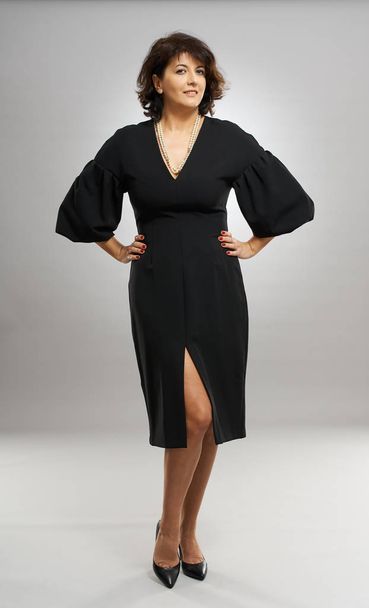 Full length of a businesswoman in black dress over gray background - 写真・画像