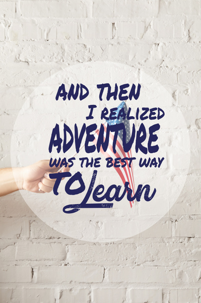 cropped image of man holding american flagpole against white brick wall with and then i realized adventure was the best way to learn quote  - Fotografie, Obrázek