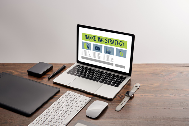 плоский lay гаджети та ноутбук з маркетингової стратегії сайт на екрані на робочому місці, ізольовані на сірому - Фото, зображення