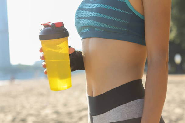 Βολή closeup της γυναίκας της γυμναστικής με αθλητικές φόρμες, κρατώντας το μπουκάλι νερό που ποζάρει στην παραλία. Χώρο για το κείμενο - Φωτογραφία, εικόνα